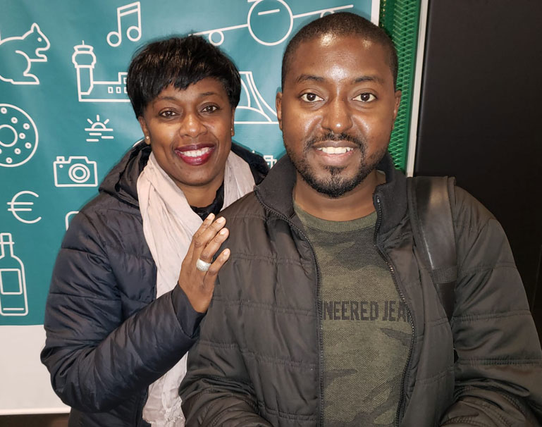 A mother with her hand on her son's shoulder, standing side by side smiling at the camera