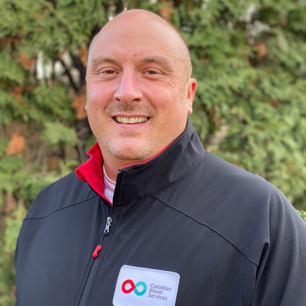 Headshot image of Aaron Barlow standing in front of a bush.