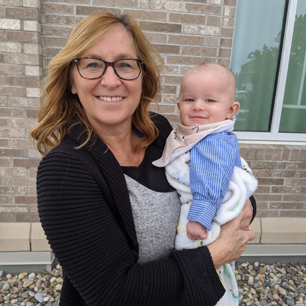 Blood donor Cori-Jo Heggie holding her grandson outside a home wearing black shirt with black glasses and blonde brunette hair