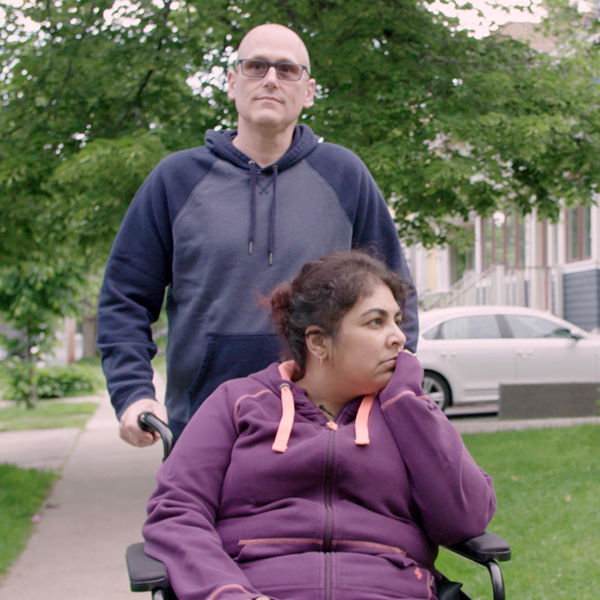 Image of Dr Shelly Sarwal in a wheelchair and Randy Tresidder behind pushing the wheelchair while going out for a stroll