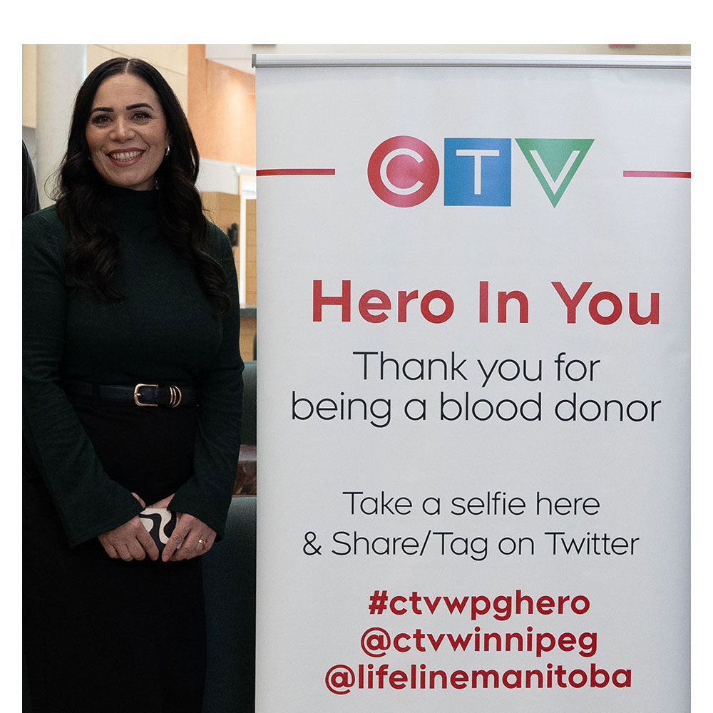 Maralee Caruso standing beside a CTV banner stand that says "Hero In You. Thank you for being a blood donor."