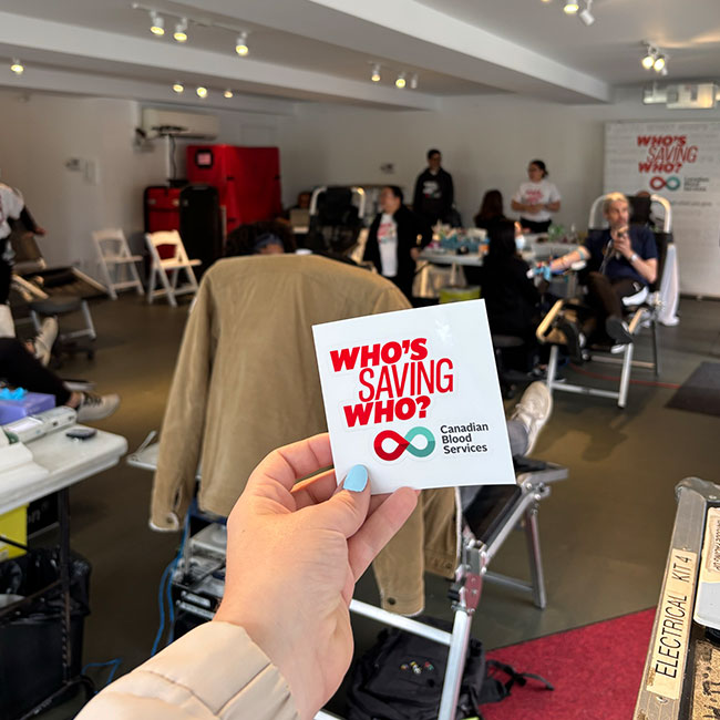 Hand holding a sticker of Who's Saving Who?