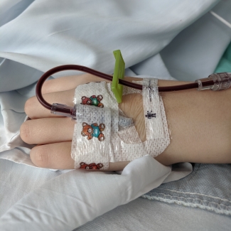 Child's hand with colourful bandage and tubes during blood transfusion