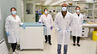 Image of Lab team members Valerie Conrod, Stacey Vitali, Andy Tshiula Kalenga and Carissa Kohnen standing in beside a freezer in the lab