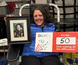 Blood donor in donor bed holding photo of sister and 50th donation sign in 