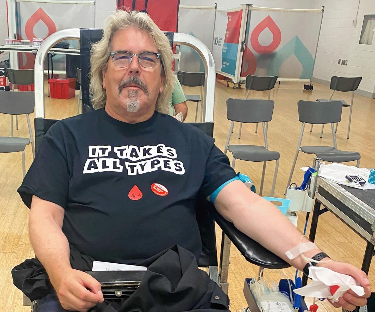 Man donating blood wearing T shirt that says "It takes all types"
