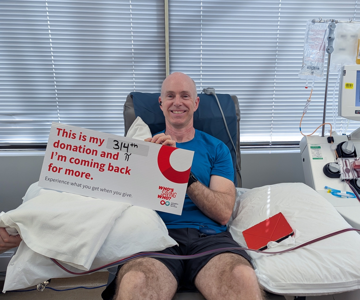 Blood donor in donor chair holding milestone donation sign