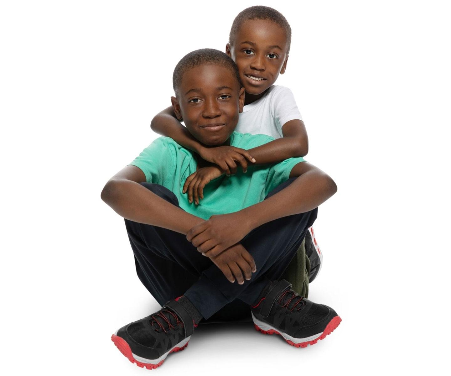 Un garçon assis les jambes croisées est enlacé par son petit frère qui se trouve derrière lui.