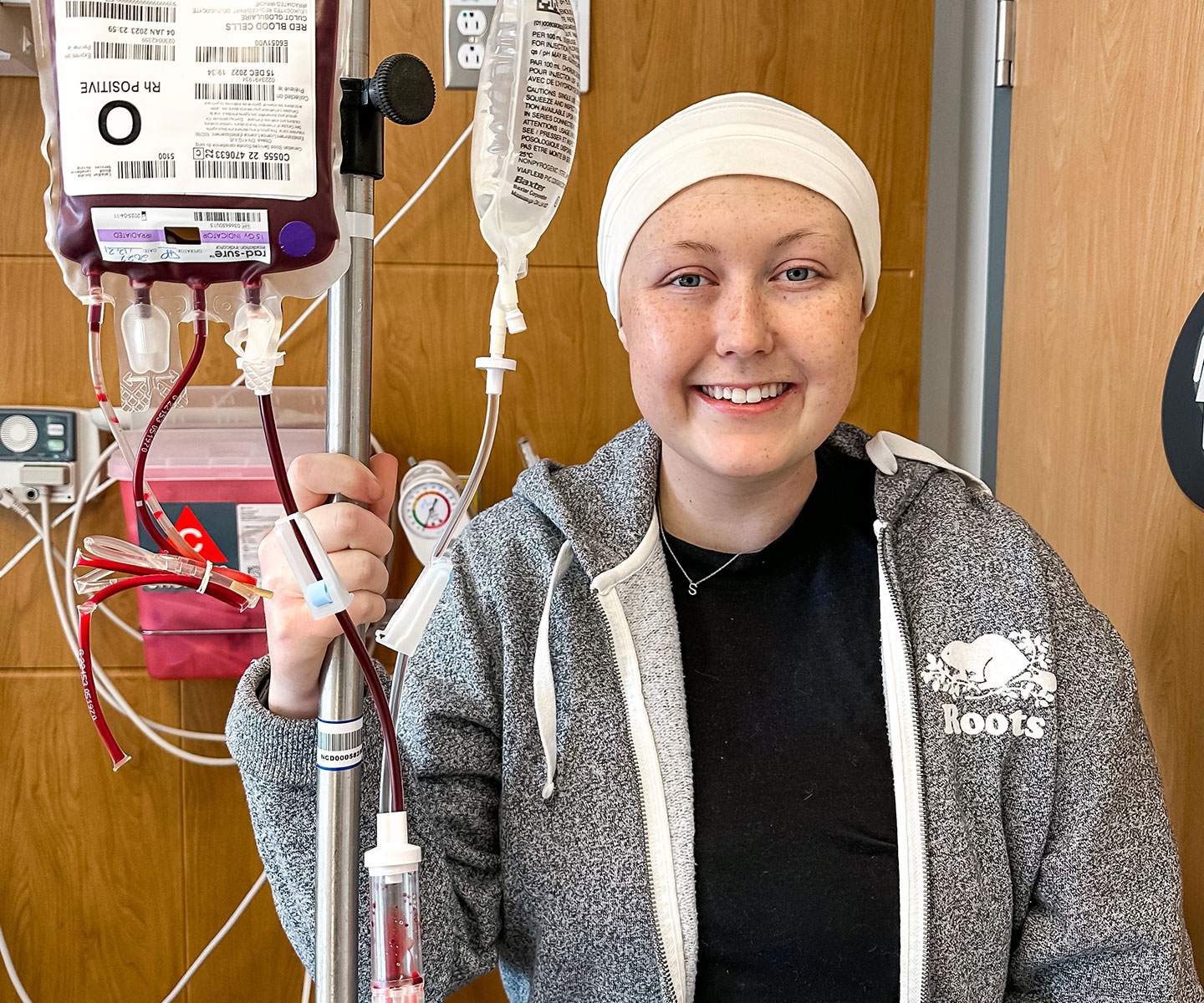 Blood recipient Shae-Lynn smiling while holding pole with blood bag during blood transfusion