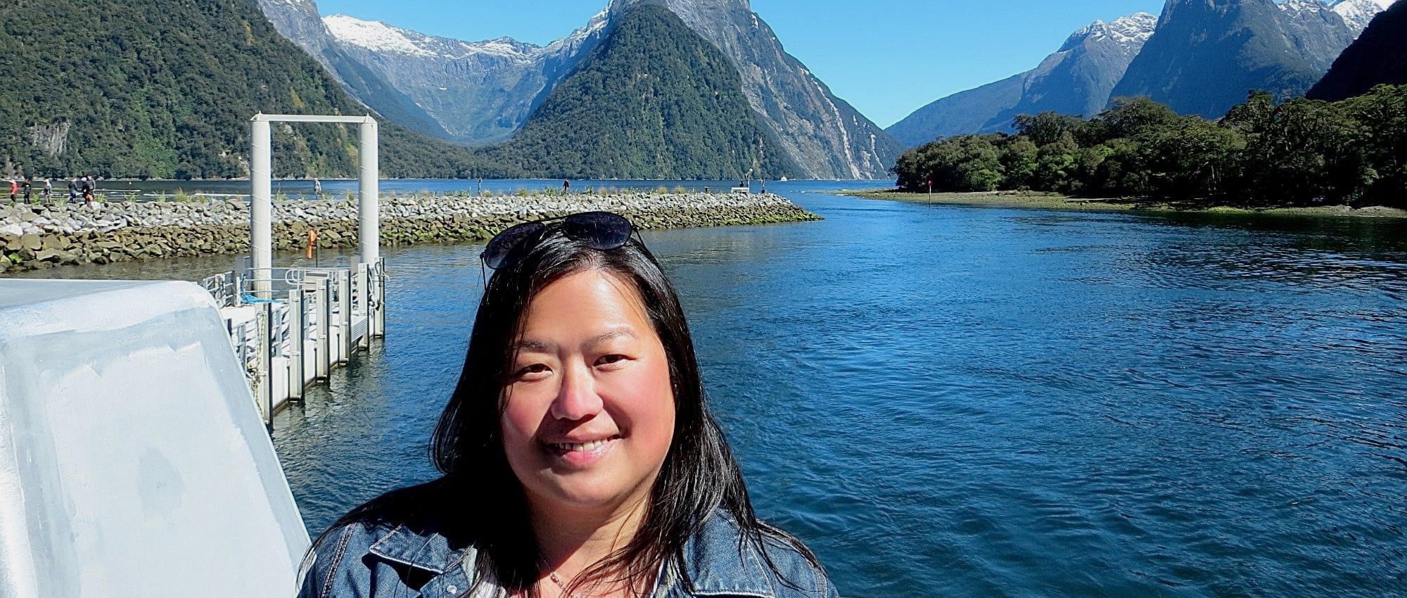 A Chinese woman stands surrounded by blue water and tall mountains.