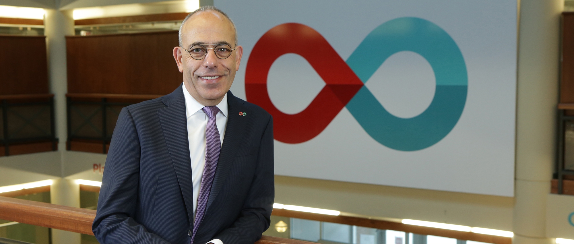 Man in suit stands in front of large sign with infinity symbol logo for Canada’s Lifeline