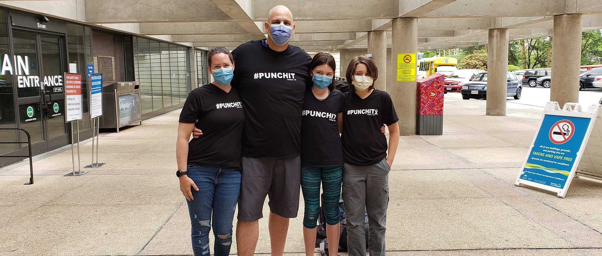 Stem cell recipient Greg Duerksen and his family give each other a side hug in front of his hospital.