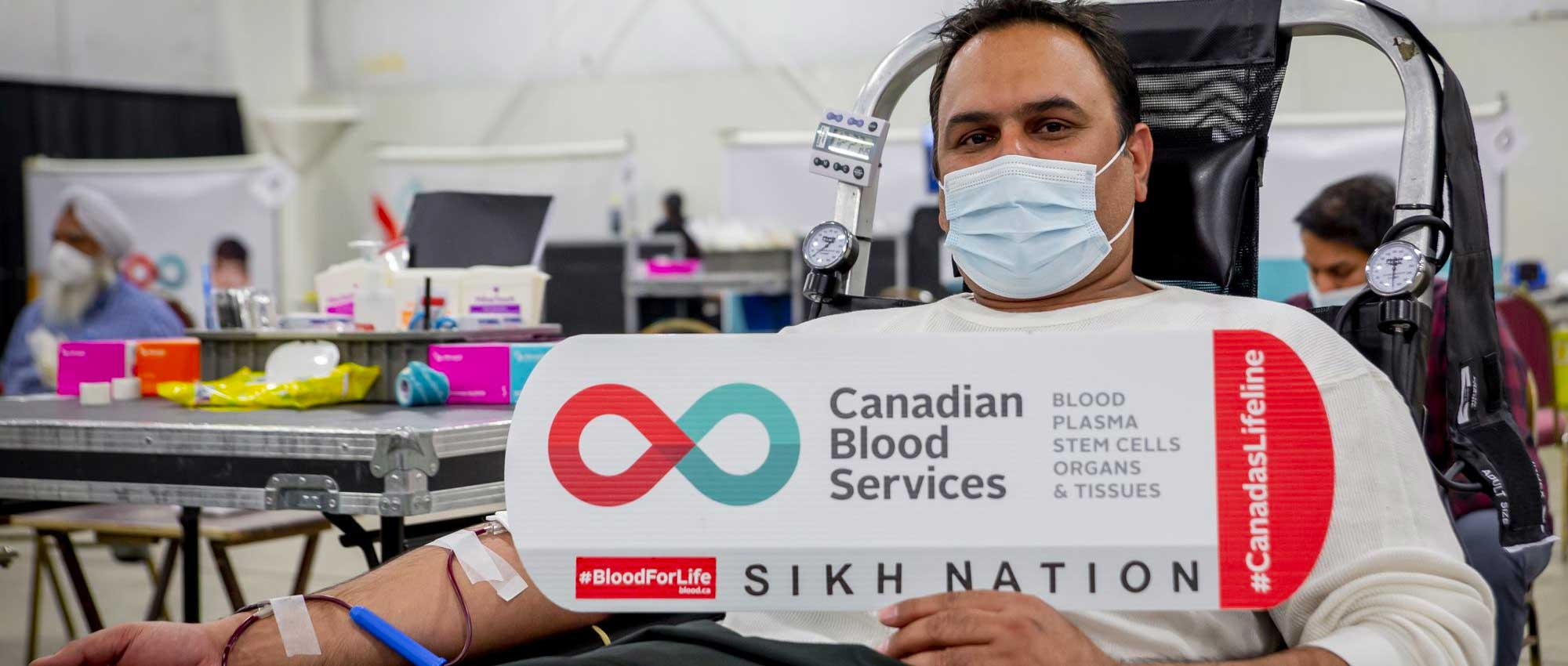 A man donating blood holding a sign that says Sikh Nation