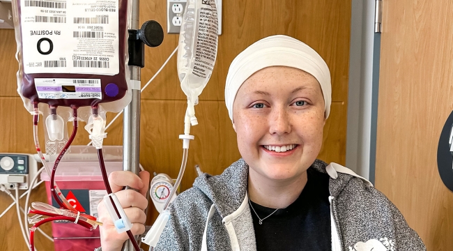 Blood recipient Shae-Lynn smiling while holding pole with blood bag during blood transfusion