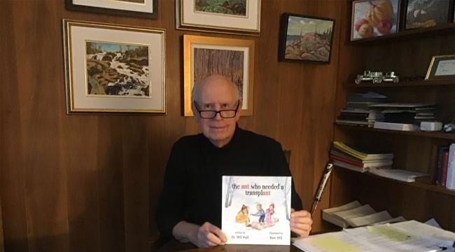 Dr Wall à son bureau tenant un exemplaire de son livre pour enfants intitulé the ant who needed a transplant.
