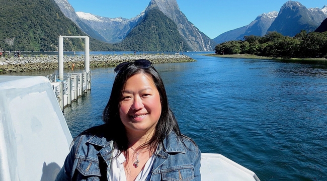 A Chinese woman stands surrounded by blue water and tall mountains.