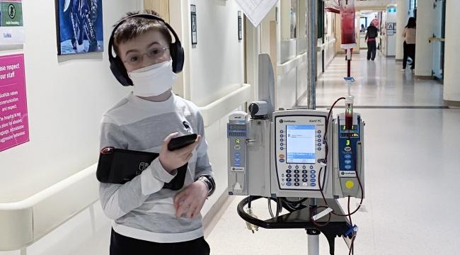 Un garçon portant des écouteurs et un masque, dans un couloir d’hôpital pendant une transfusion