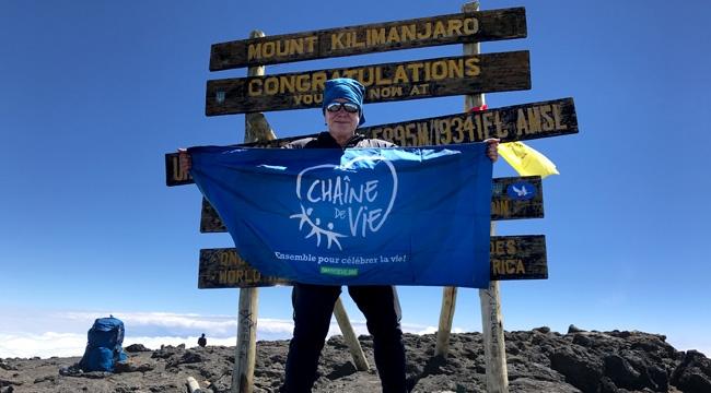 Lucie Dumont stands on top of Mount Kilimanjaro holding the Chain of Life flag.