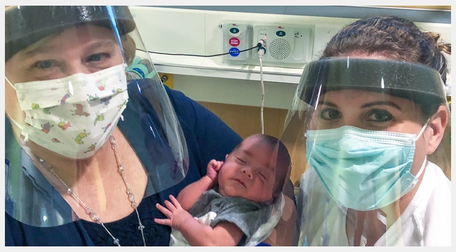 Close up image of Nurse practitioner Carolyn Kelly, Anna Patten and her infant son John-Derrick who required a blood transfusion. Both Carolyn and Anna are wearing masks and shields.