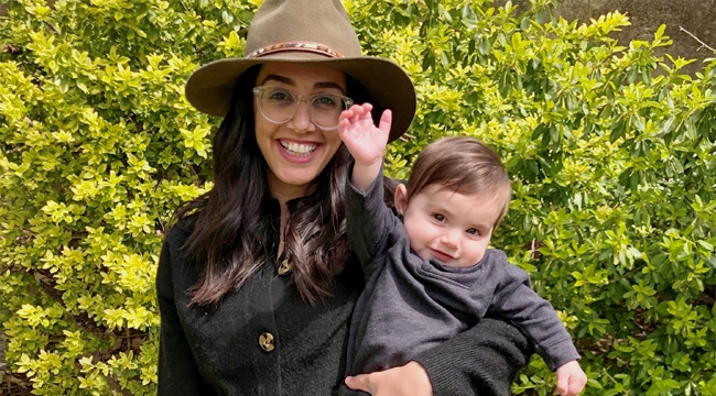 A young woman in a wide-brimmed hat smiles broadly as she holds her baby son.