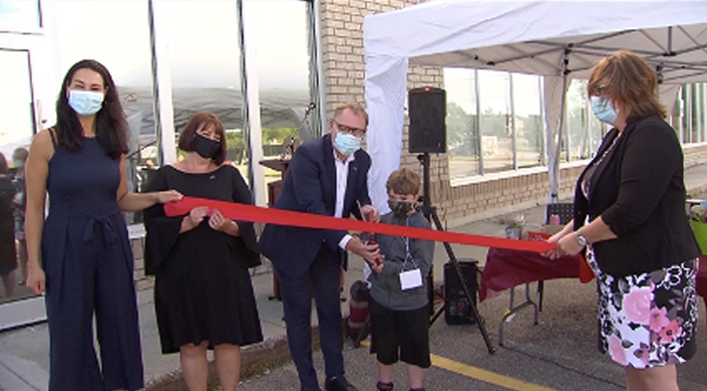 Image of Vice President of Plasma Jean-Paul Bédard and Heydan Morrison holding a pair of large scissors cutting the ribbon for the temporary opening of Sudbury Plasma Centre