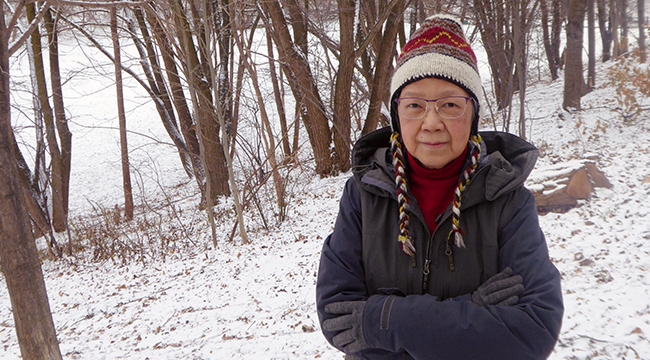 A woman in winter coat and hat standing in a snowy wooded area