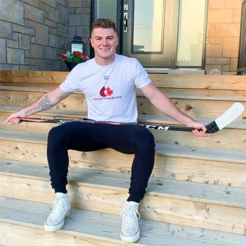 Image of blood donor and registered organ donor Liam Peyton sitting outside on the front steps holding a hockey stick on his lap