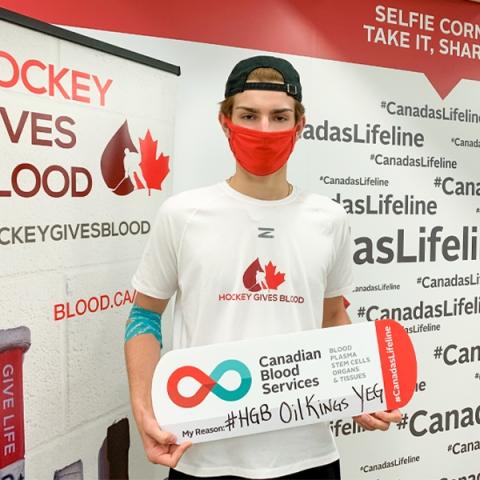 Blood donor and registered organ donor Sebastian Cossa holding a my reasons sign wearing a white Hockey Gives Blood t-shirt